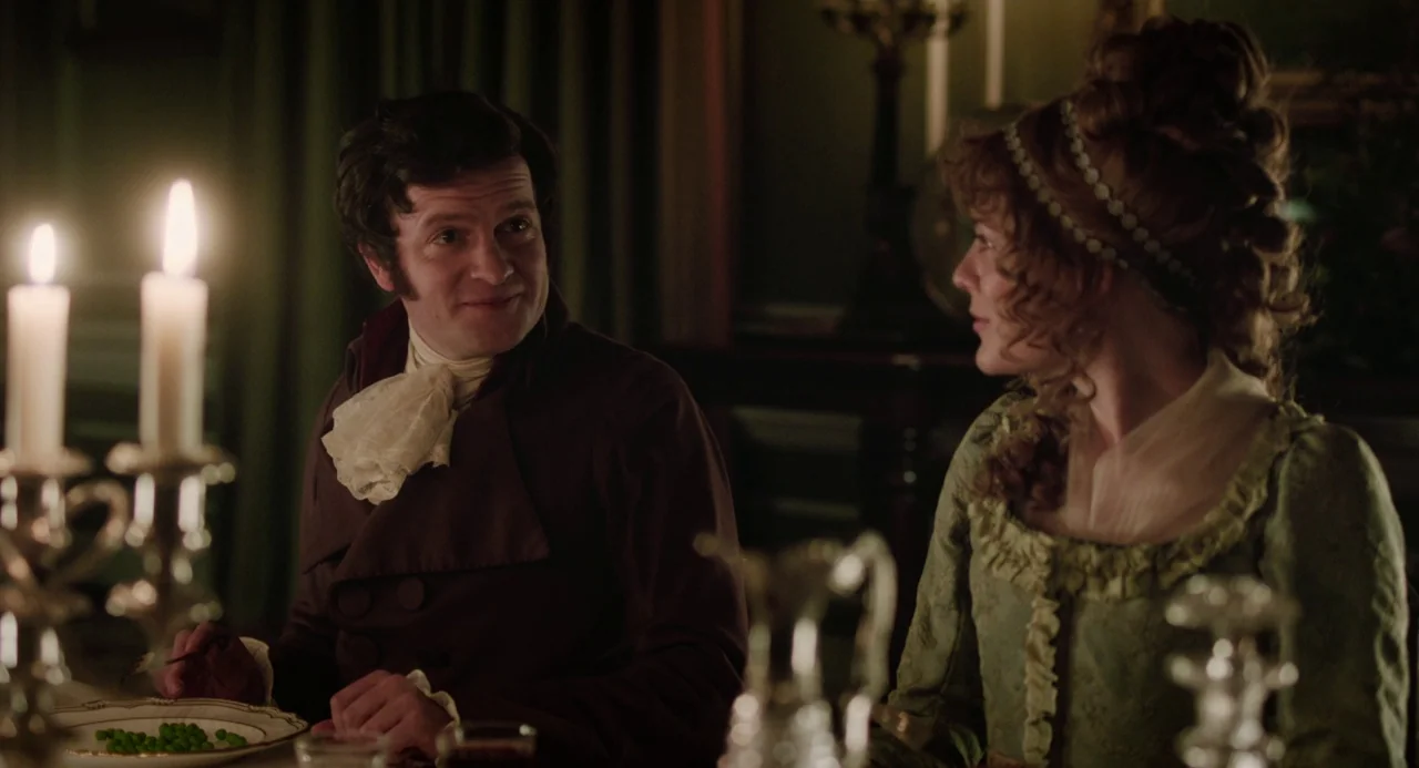 Love and Friendship (2016) movie still: medium — A dimly lit room in an 1800s manor features a formal dinner table setting. A man eats from a plate…