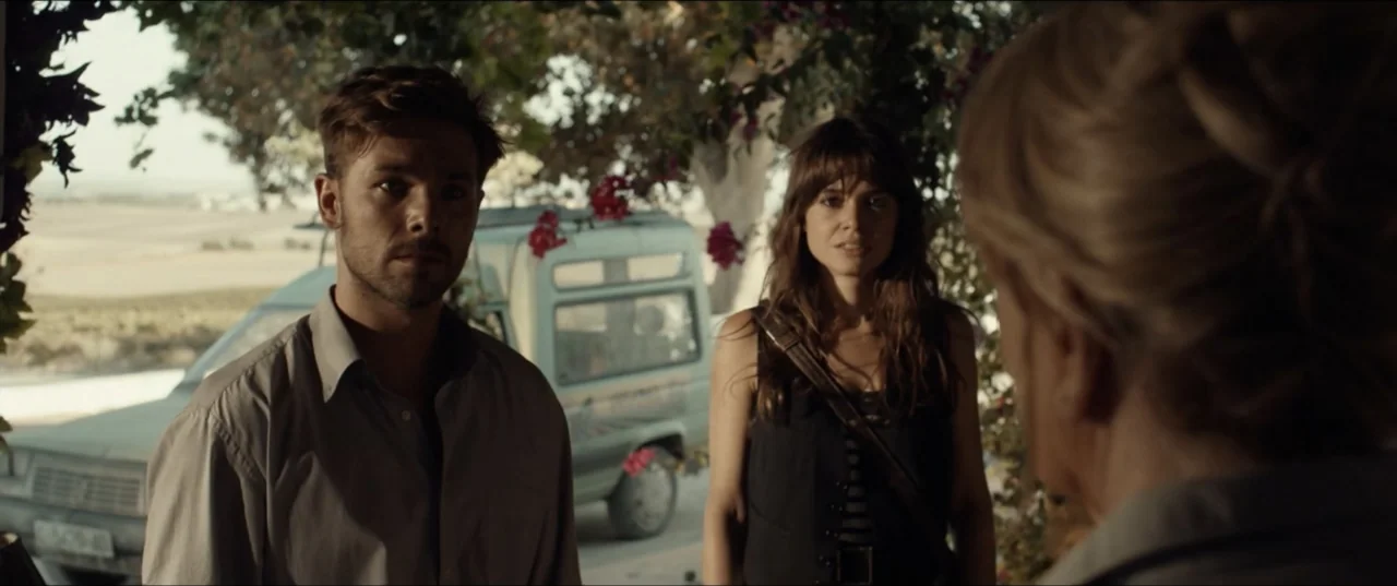 Hear Me: Our Summer (2024) movie still: medium — A shaded patio with hanging bougainvillea and a parked van in the background. Three people stand…