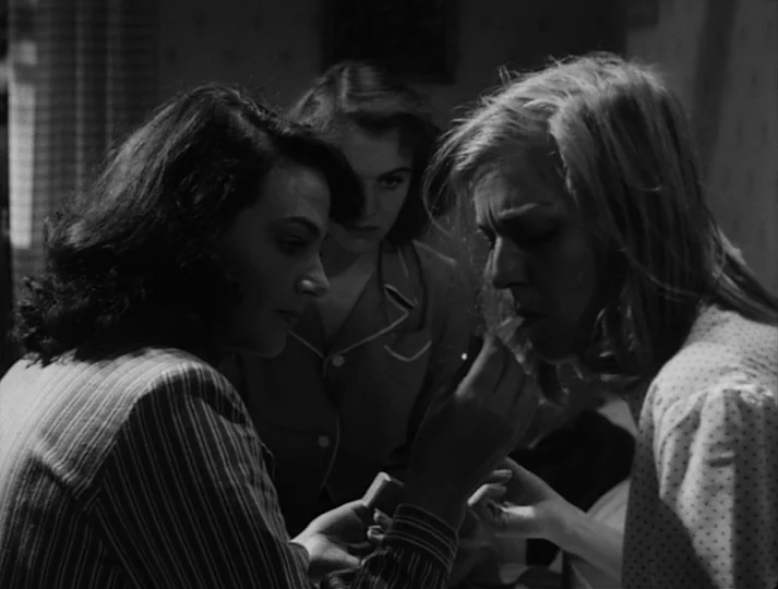 Port of Call (1948) movie still: medium — Three women gather in a dimly lit room with patterned wallpaper. One woman applies makeup to another's…