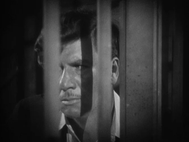 Underworld (1927) movie still: closeup — A dark, cramped space marked by heavy vertical metal bars in the foreground. A man stands behind the bars…