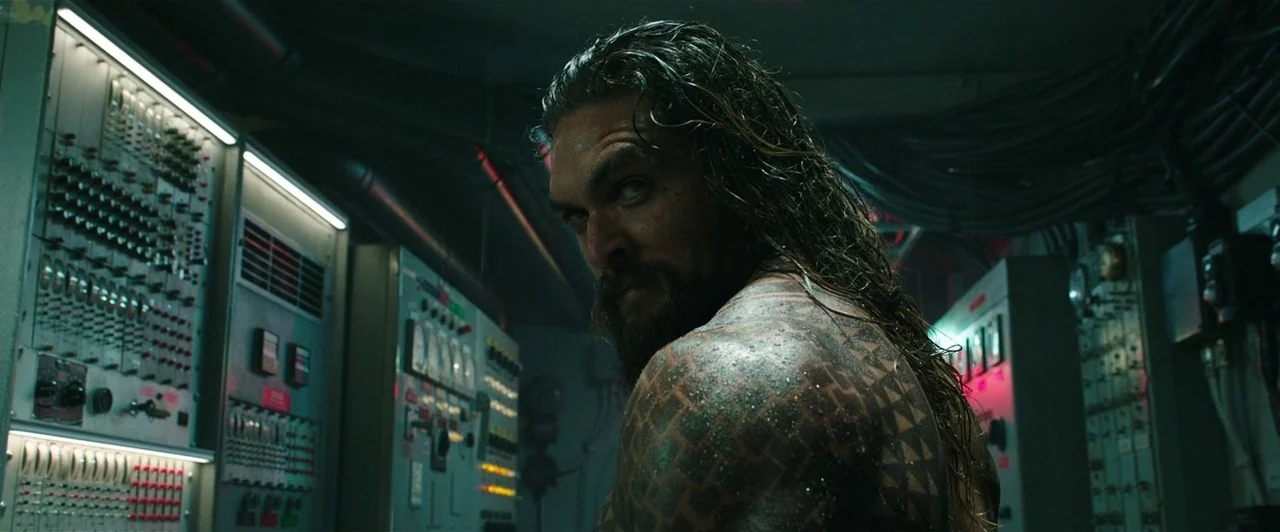 Aquaman (2018) movie still: medium — A cramped technical space filled with industrial control consoles and exposed wiring conduits. A muscular man…