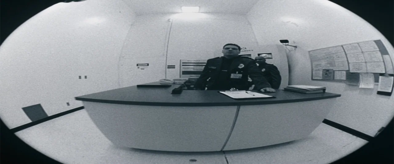 The Eraser (1977) movie still: medium — A stark white security booth features a wide desk and high ceilings. Two uniformed security guards stand…