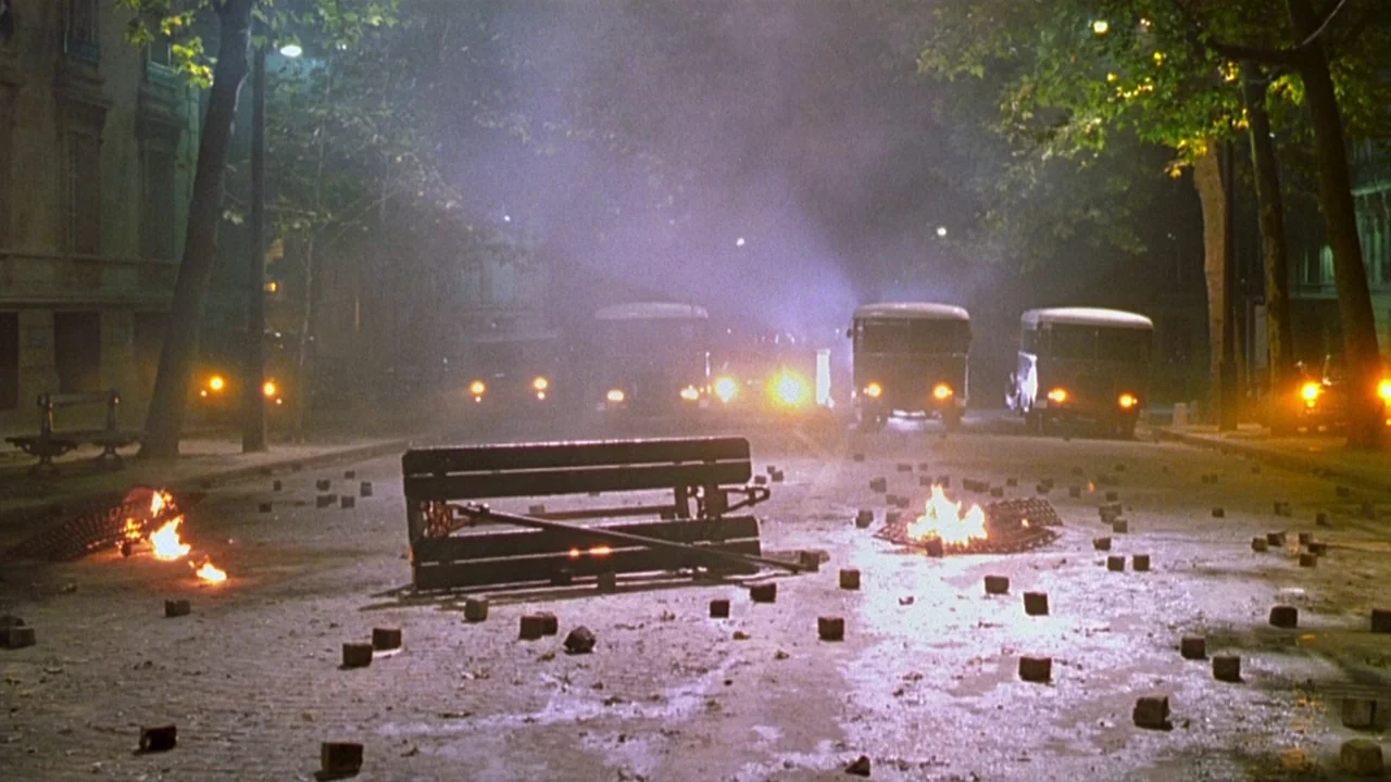 The Dreamers (2003) movie still: wide — A city street at night is cluttered with cobblestones and burning debris piles. Several dark utility…