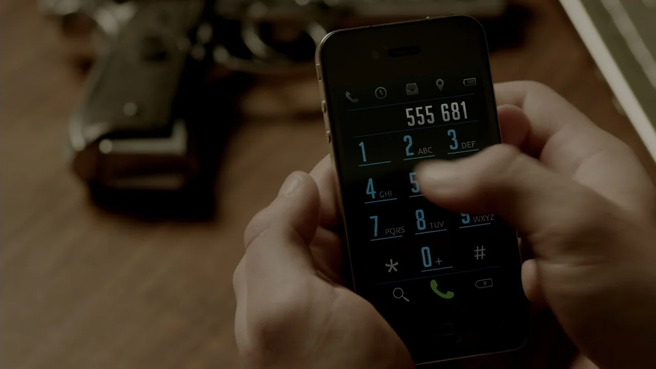 6 Bullets (2012) movie still: closeup — A close-up shot focuses on hands operating a smartphone with a glowing numerical dialer. A handgun sits out…