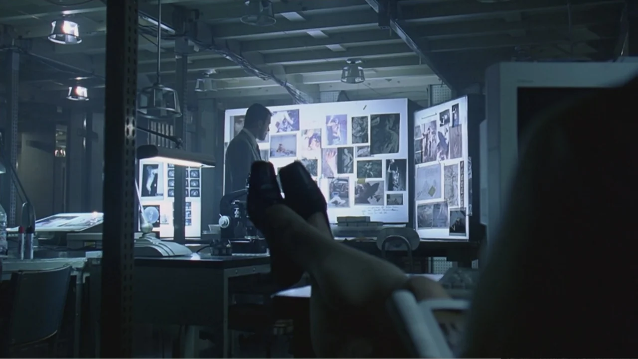 Hannibal (2001) movie still: medium — A dark, cluttered forensic lab features a large illuminated board covered in crime scene photographs. A man…