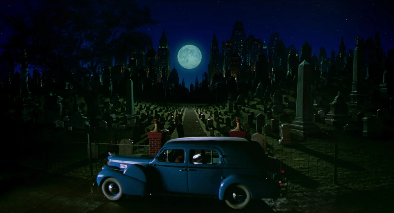 Dick Tracy (1990) movie still: wide — A dark cemetery with rows of weathered headstones sits before a glowing full moon. A vintage blue sedan is…