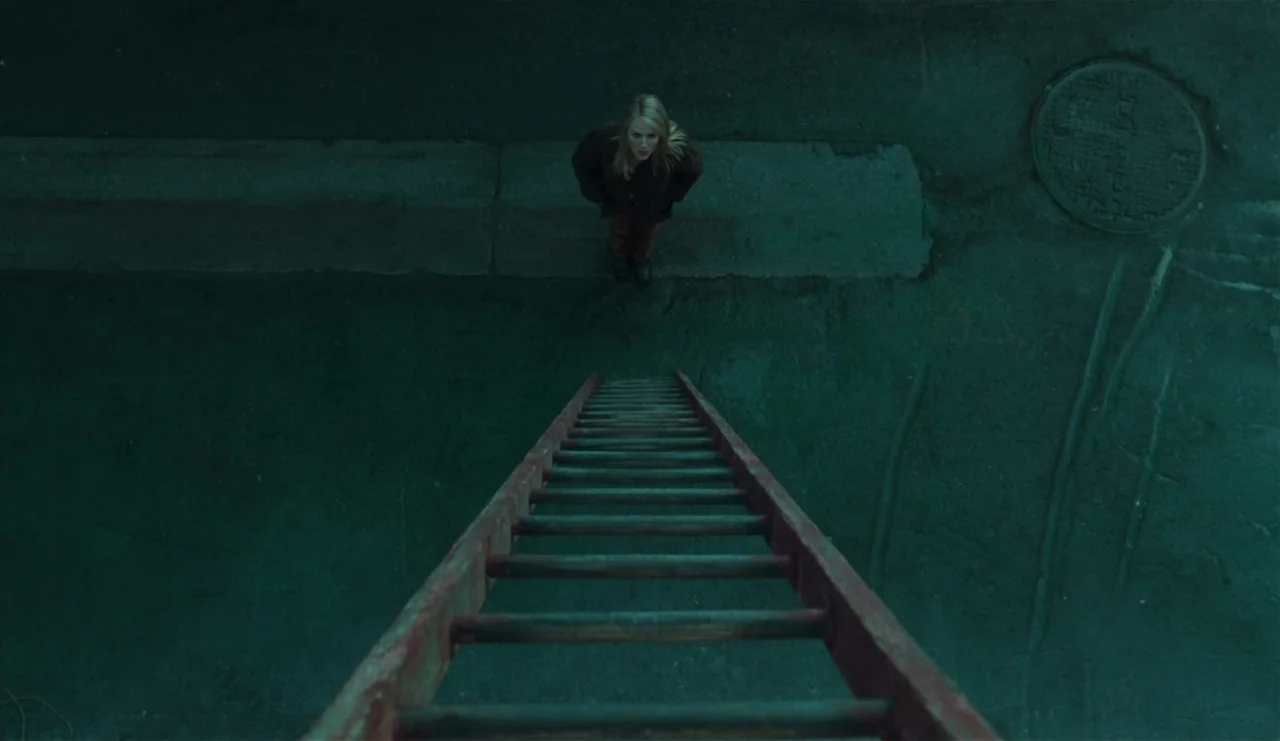 The Ring (2002) movie still: wide — A dark, empty alleyway with wet pavement and a visible circular manhole cover. A woman stands on the ground…