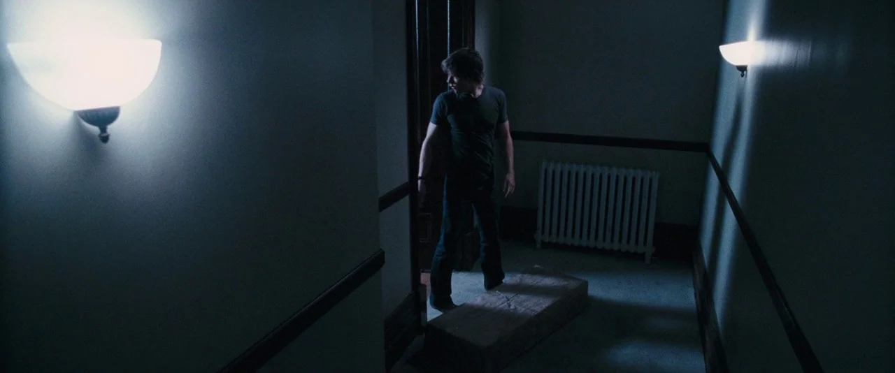 Dead Silence (2007) movie still: wide — A dimly lit residential hallway features two bright wall sconces and a white radiator. A man in dark…