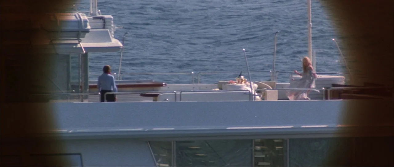 Never Say Never Again (1983) movie still: wide — The white deck of a large yacht is surrounded by dark blue open water. A man and a woman stand…