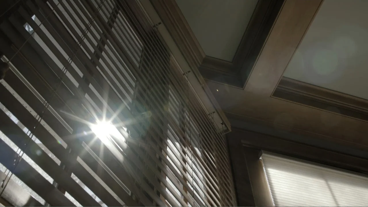 A Gift from God (2019) movie still: establishing — An interior space features wooden blinds covering a window with bright sunlight behind them.…