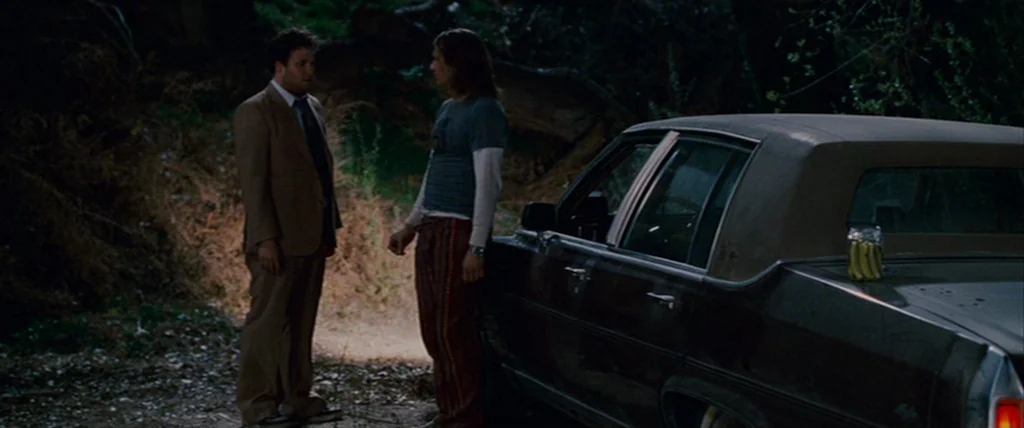 Pineapple Express (2008) movie still: fullbody — Two men stand together in a dark dirt lot at night next to a car. One man wears a suit while the…