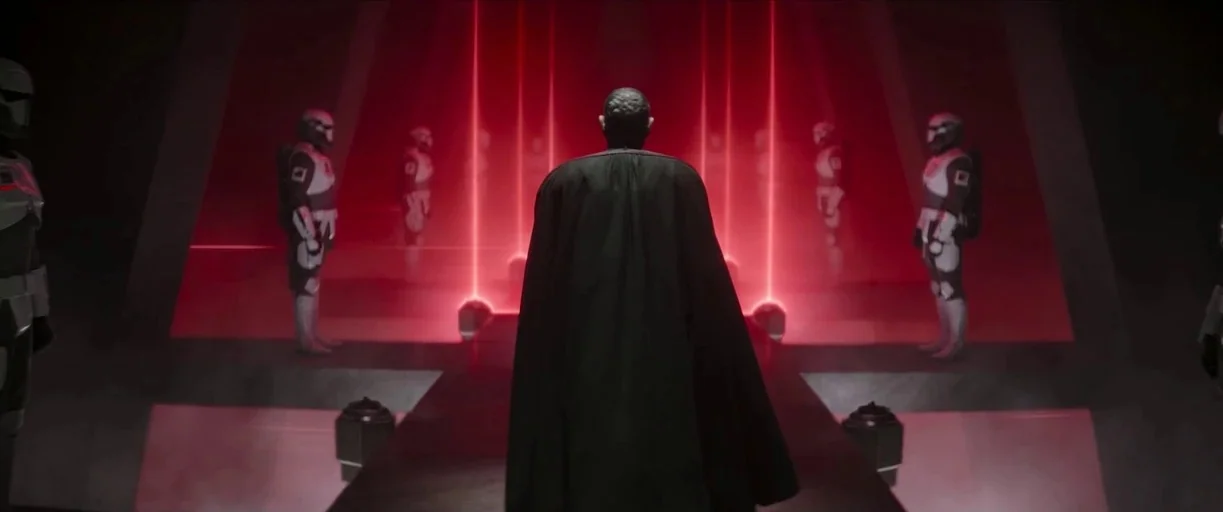 The Mandalorian (2019) movie still: fullbody — A dark, symmetrical command room features a raised walkway between vertical red light beams. A man in…