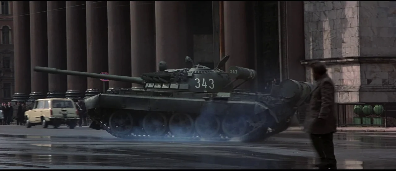 GoldenEye (1995) movie still: wide — A military tank parked on a wet city street in front of a classical building. A man walks past the tank in the…