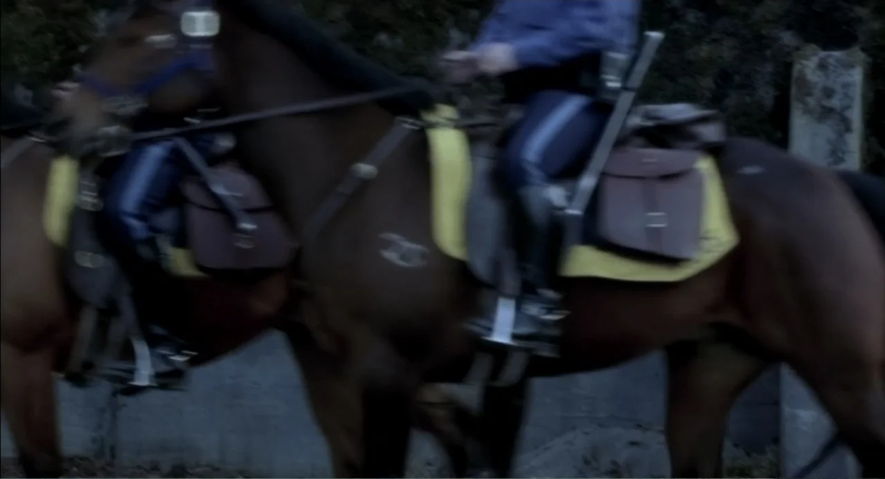 The Hunted (2003) movie still: medium — Two mounted police officers ride horses along a dark, dimly lit outdoor path. Motion blur obscures the…