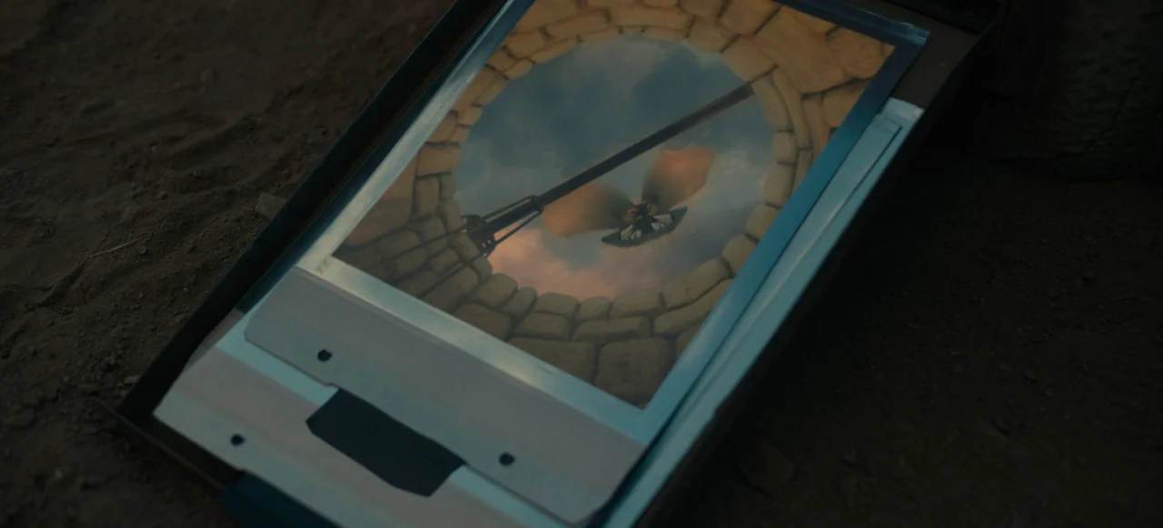 Nope (2022) movie still: closeup — A close-up shot of a photograph lying face up on dark, dry dirt. The photograph shows a stone-lined well looking…