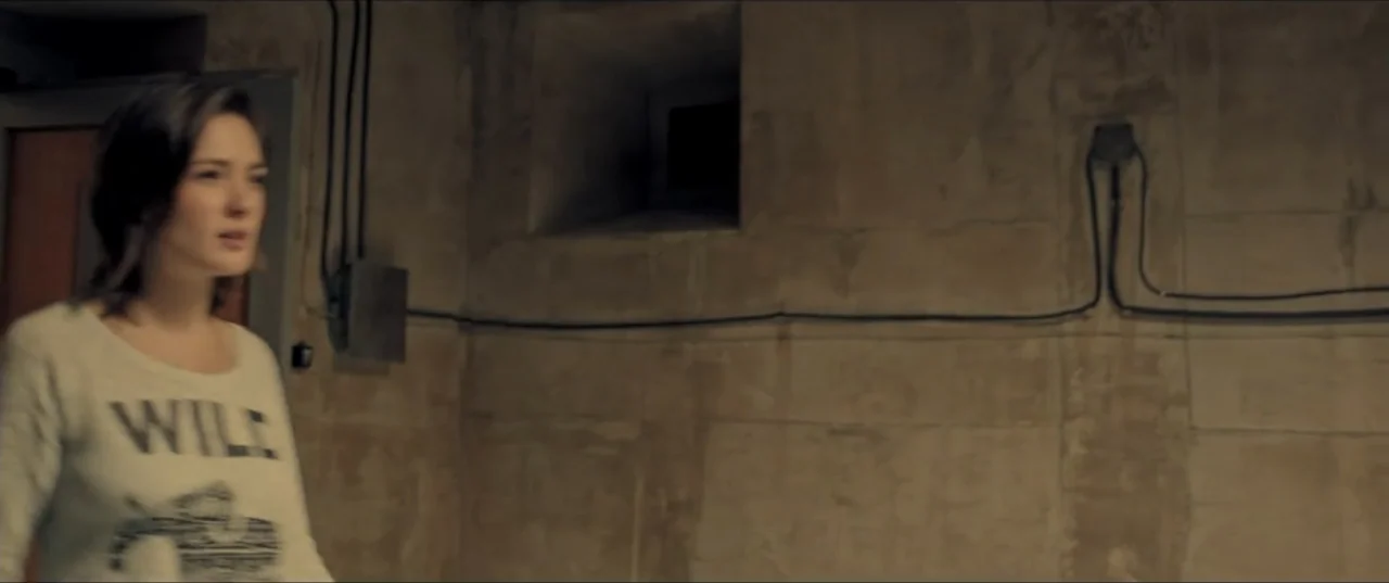 Room 6 (2006) movie still: medium — A windowless room features unfinished poured concrete walls with exposed electrical conduits running across…