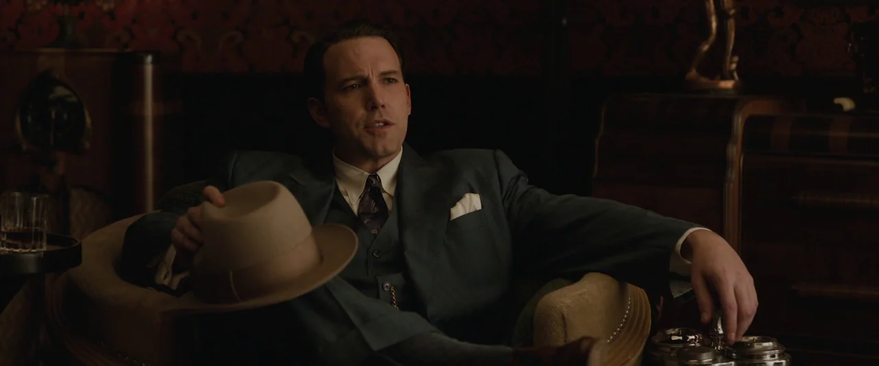Live By Night (2016) movie still: medium — A dark study features ornate red patterned wallpaper and polished wooden furniture. A man in a tailored…