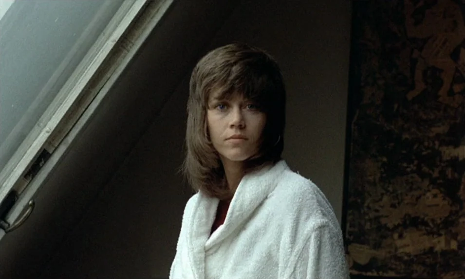 Tout Va Bien (1972) movie still: medium — A woman stands indoors near an angled ceiling window that provides daylight. She gazes directly into the…