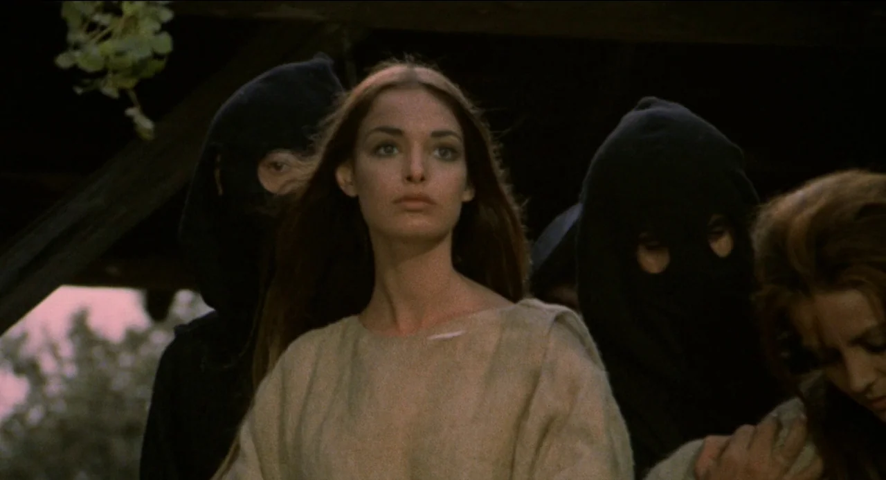 Beatrice Cenci (1969) movie still: medium — A group of people stands outdoors under a dark wooden structure. A young woman in a beige tunic is…
