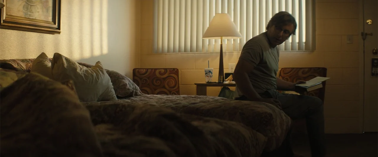Those Who Wish Me Dead (2021) movie still: medium — A dated motel room features patterned bedding, block walls, and vertical window blinds. A…