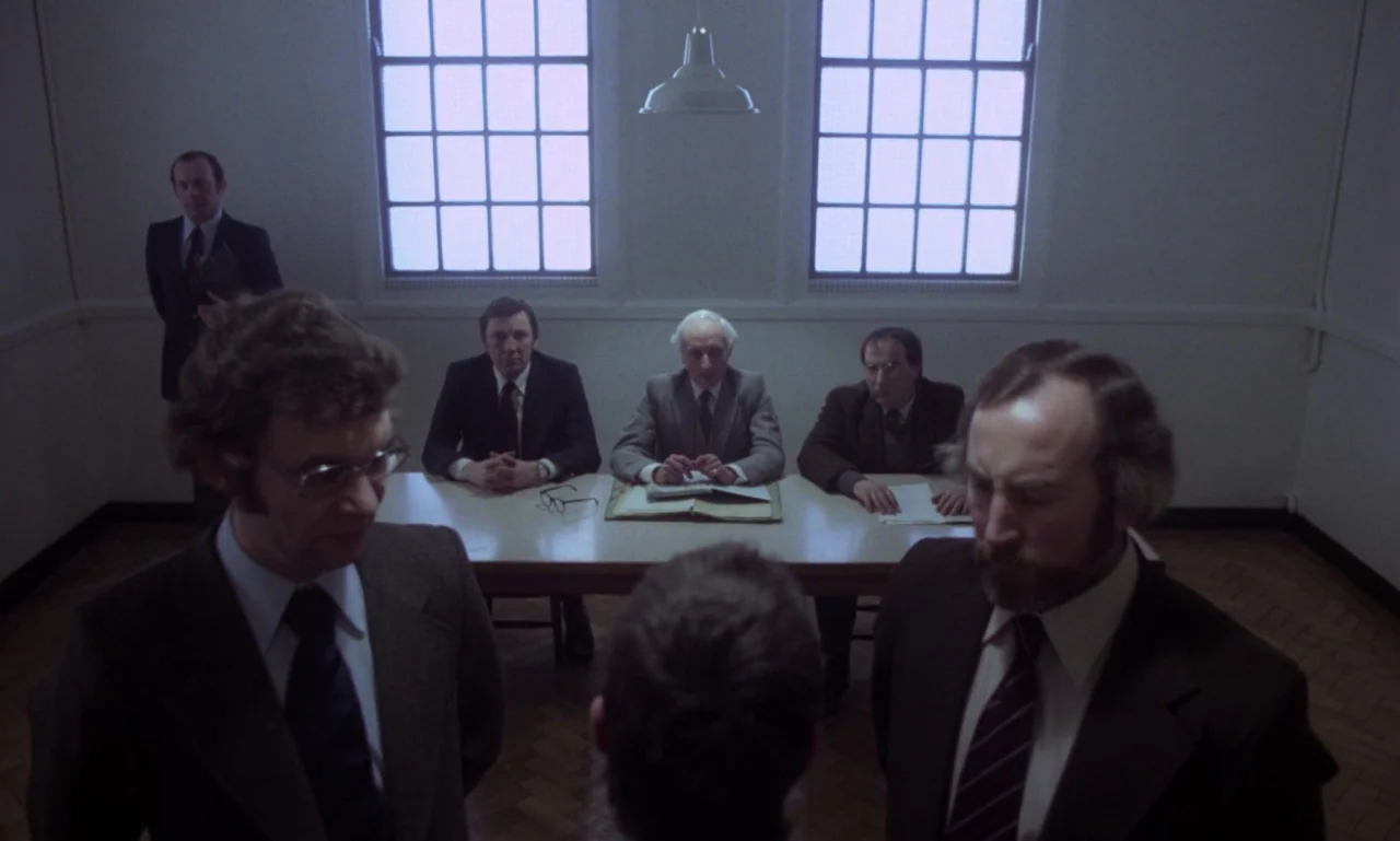 Scum (1979) movie still: wide — An austere room features plain light walls, two large grid windows, and parquet flooring. Multiple men wearing…