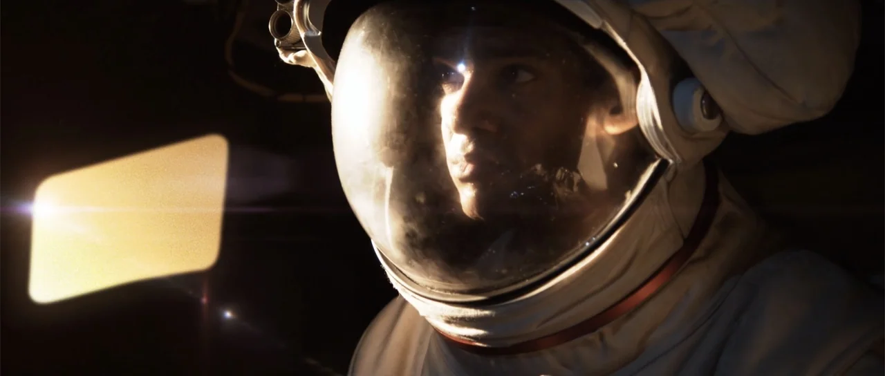 Astronaut: The Last Push (2012) movie still: closeup — A cramped interior of a spacecraft cockpit features a man in an astronaut suit. The man gazes…