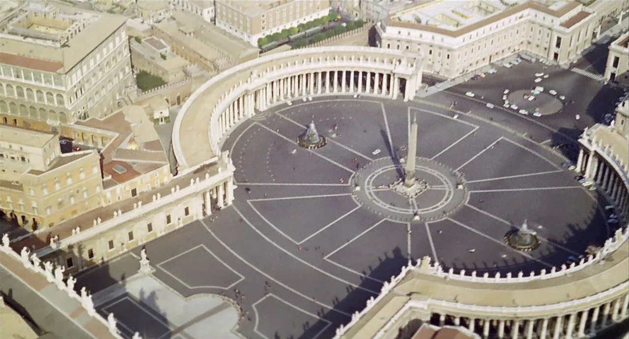 The 10th Victim (1965) movie still: establishing — A wide aerial view of St. Peter's Square with its distinctive colonnades and central obelisk. The…