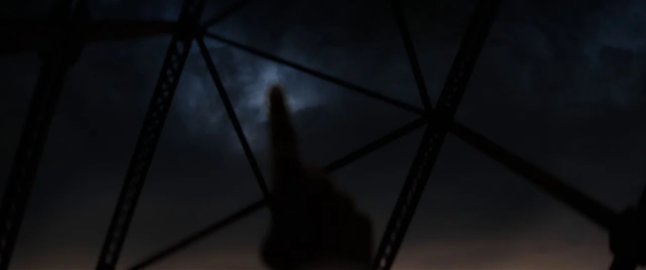 The Empty Man (2020) movie still: closeup — A dark, blurry silhouette of a finger is centered against a cloudy night sky. The foreground features…
