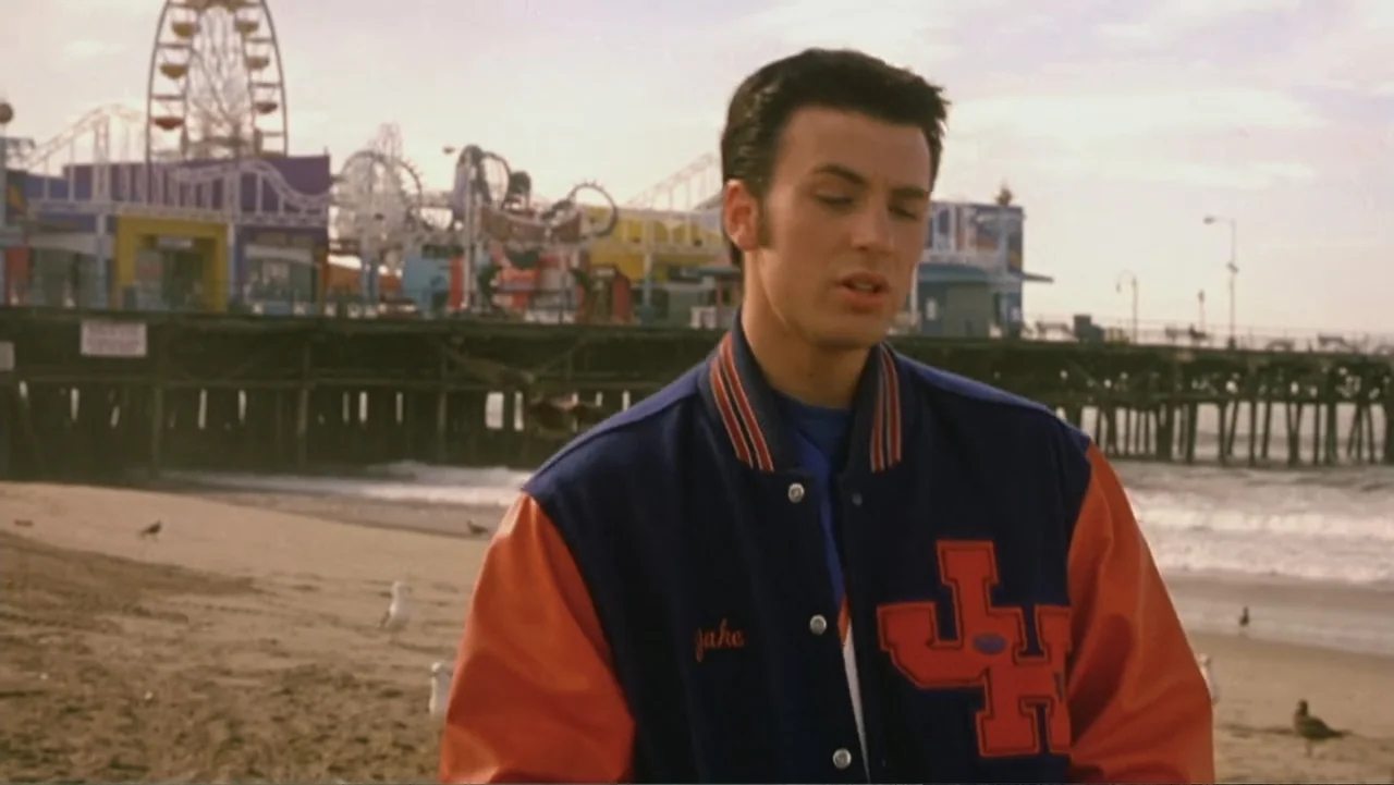 Not Another Teen Movie (2001) movie still: medium — A sandy beach sits beneath a wooden pier featuring an amusement park ride. A young man in a…