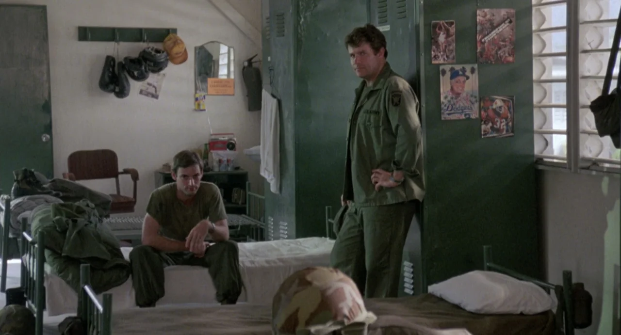 American Ninja (1985) movie still: medium — A military barracks room features green metal lockers, bunk beds, and posters on walls. Two men in…