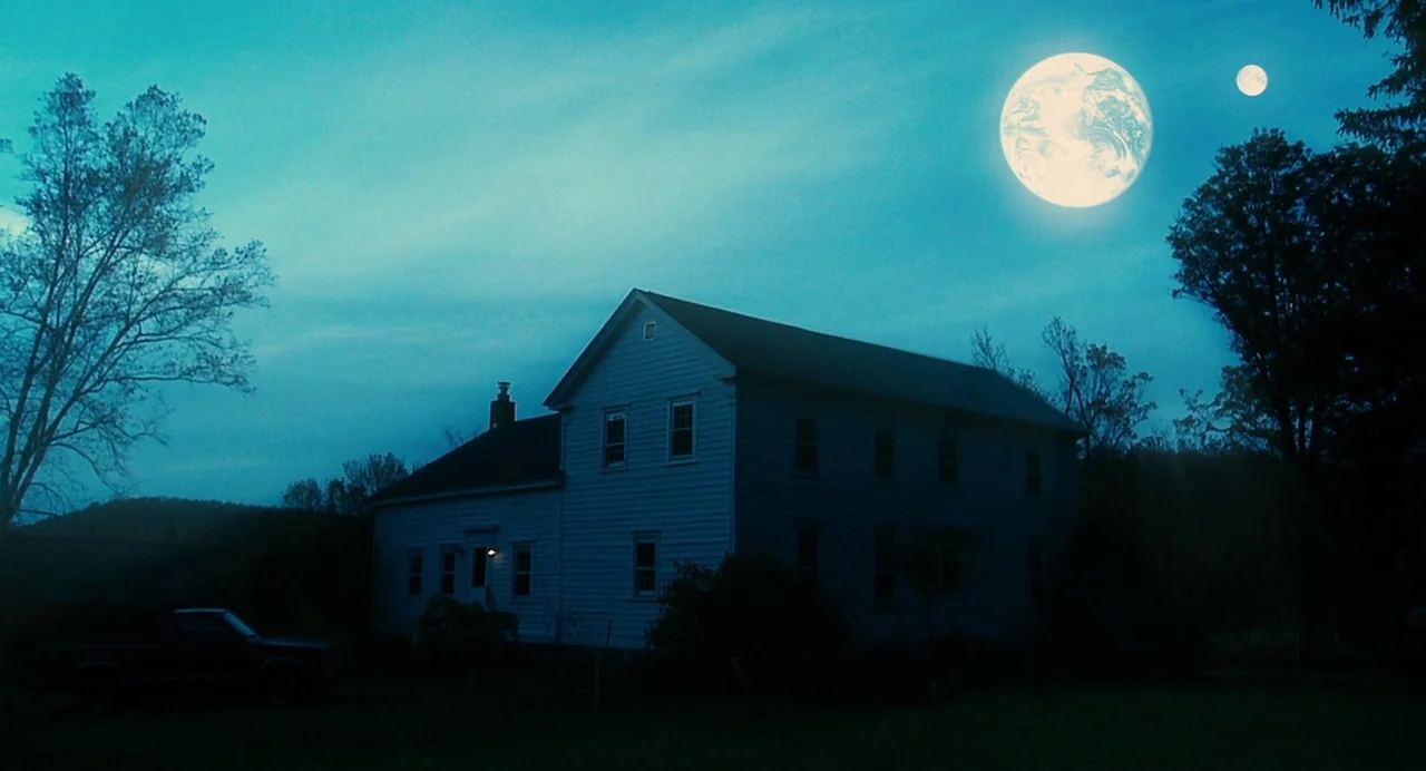 Another Earth (2011) movie still: wide — A rural white farmhouse stands on a dark property under a twilight sky. Two celestial bodies, one appearing…