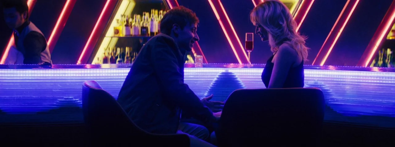 Dead Pigs (2018) movie still: medium — A dark, modern nightclub bar features glowing blue counter edges and triangular red neon accents. A man and a…