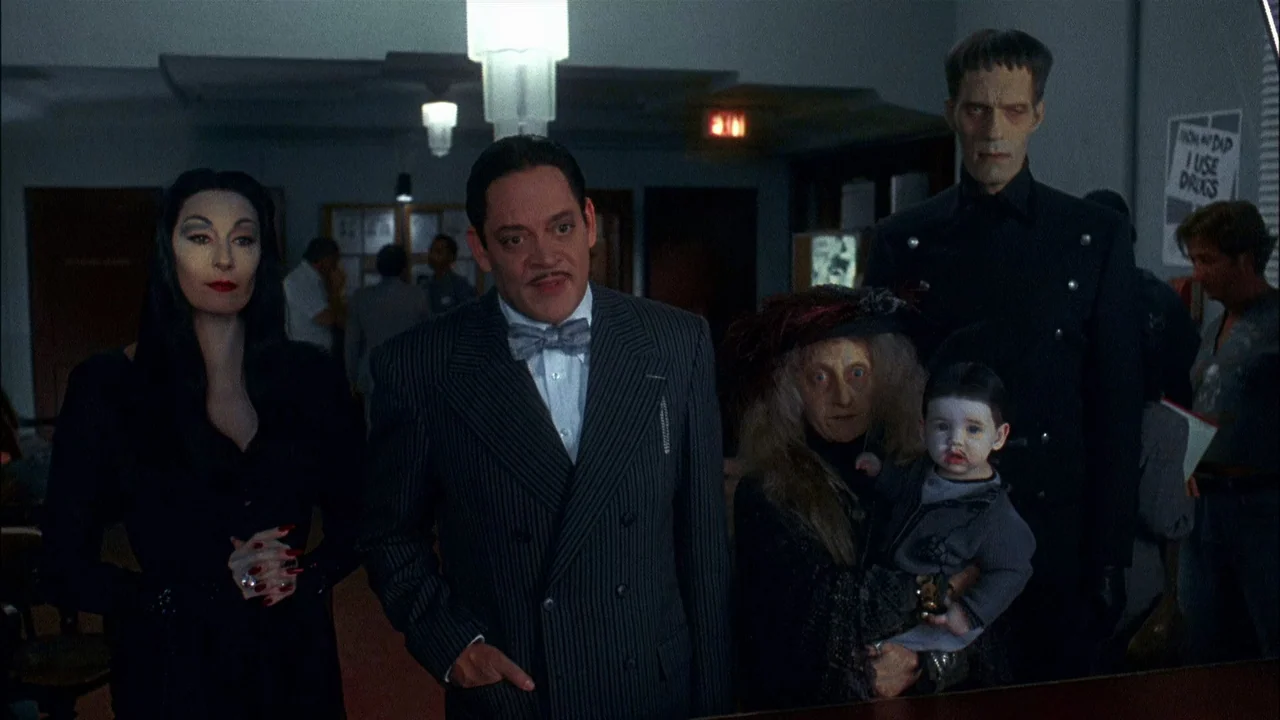 Addams Family Values (1993) movie still: medium — An administrative room features drop-ceiling lights and neutral-colored walls with posted notices.…