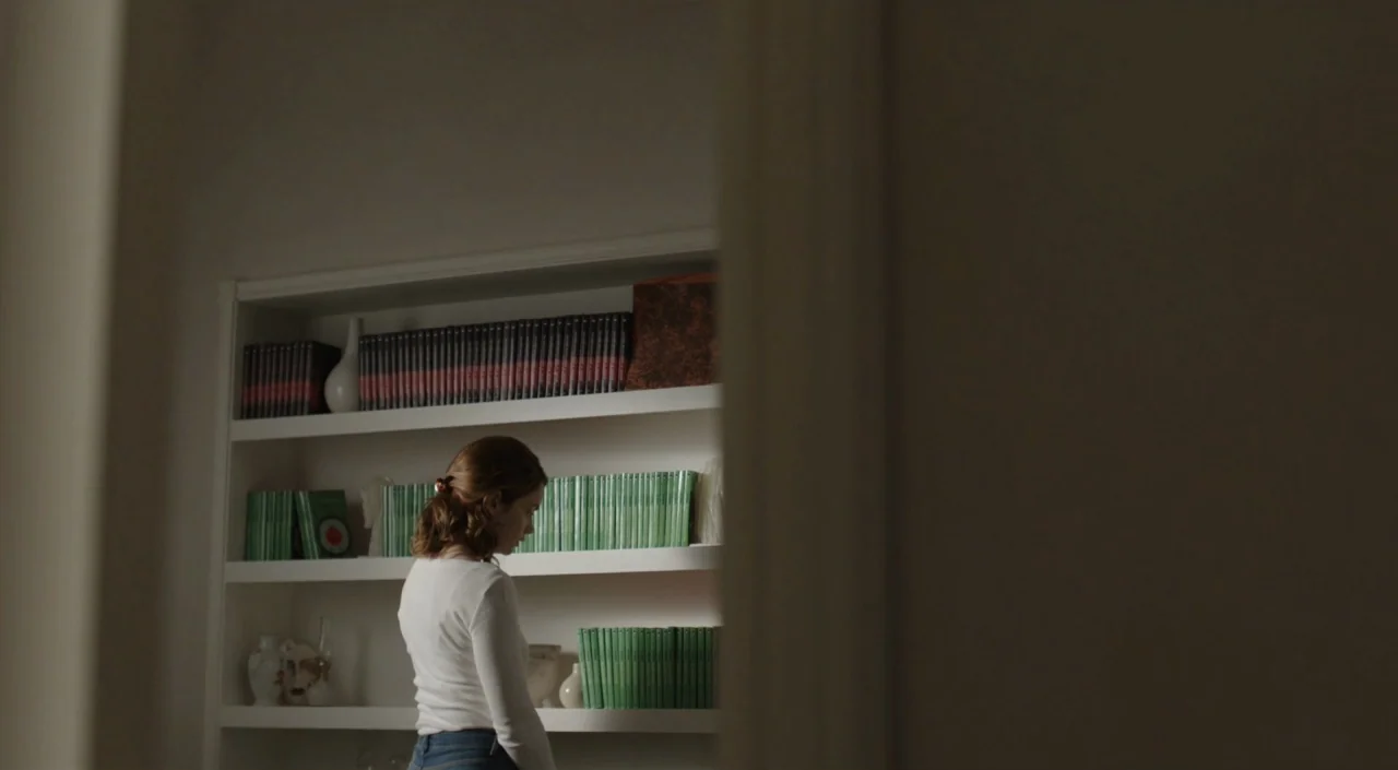 I Am The Pretty Thing That Lives In The House (2016) movie still: medium — A white built-in shelving unit displays rows of green and black books in…