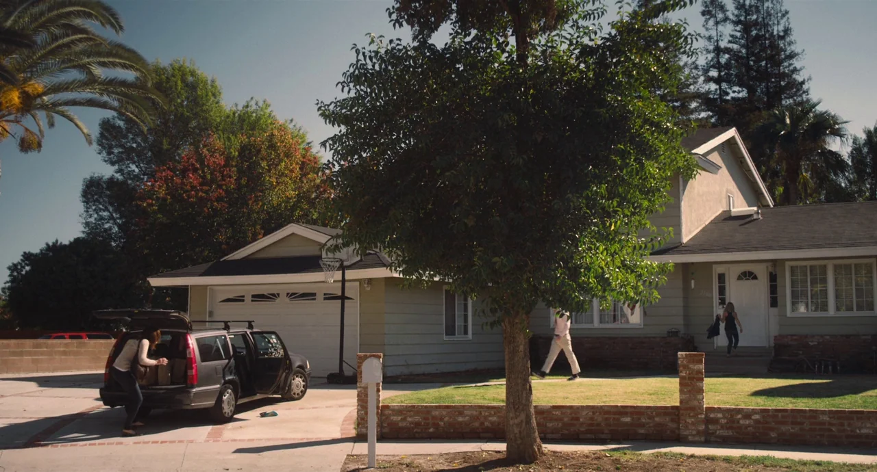 Palo Alto (2013) movie still: wide — A suburban residential street features a single-story house with a white garage door. A person removes items…