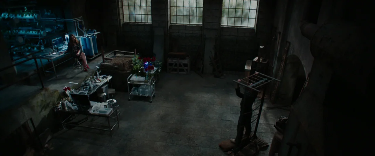 Iron Man 3 (2013) movie still: wide — A dimly lit industrial basement serves as a makeshift laboratory with concrete walls. One person works at a…