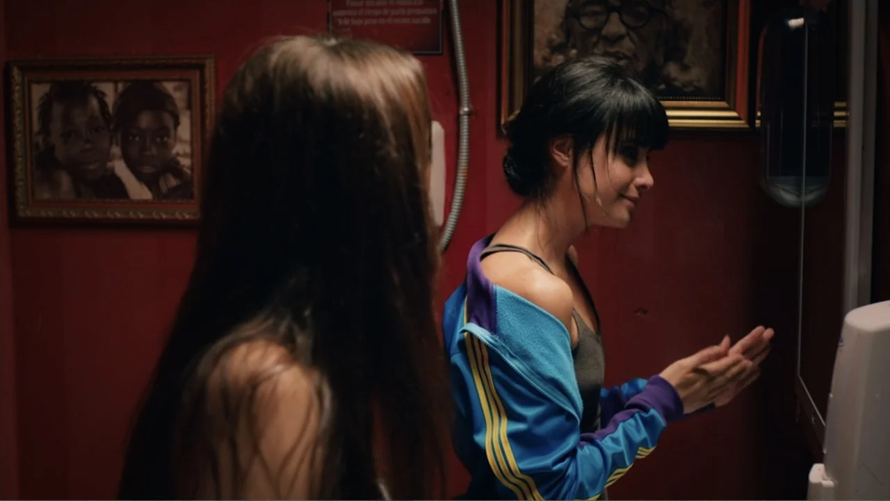 Alice in Marialand (2014) movie still: medium — A dimly lit room with dark red walls decorated with framed portraits of people. Two women occupy the…