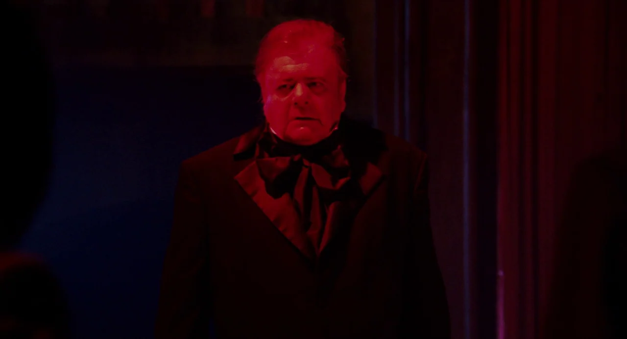 Repo! The Genetic Opera (2008) movie still: medium — A dimly lit indoor space is bathed in a distinct red light source. An older man dressed in a…