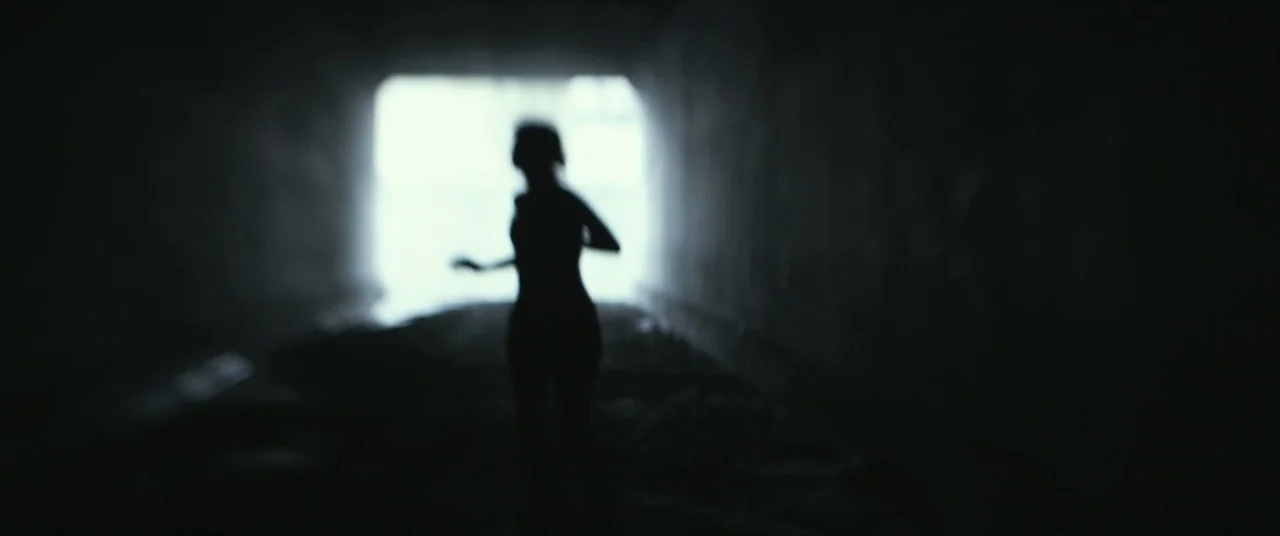 Maniac (2012) movie still: medium — A dark, shadowed underpass with a bright light source at the far end. A female figure runs toward the viewer…