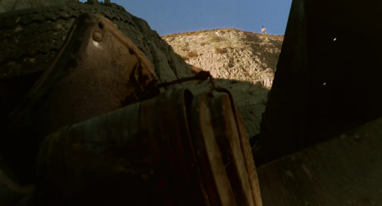 Duel (1971) movie still: wide — A pile of rusted, discarded metal junk and old tires fills the dark foreground. In the distant background, a single…