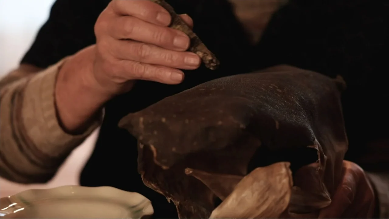 Alien Sharks: Ghosts of Japan (2024) movie still: closeup — An interior space with a person working on a dark textured organic item. The person's…