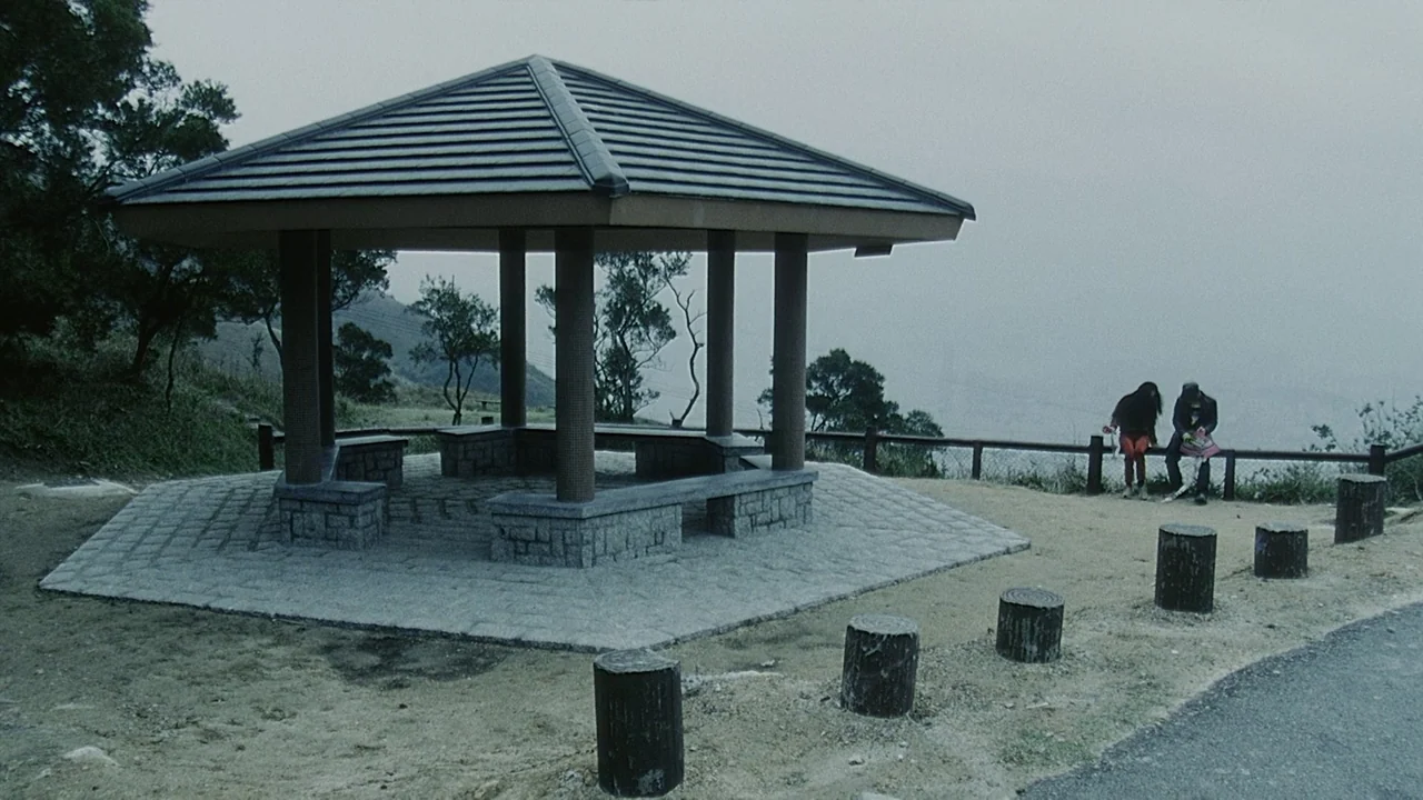 Visible Secret (2001) movie still: wide — A stone-paved gazebo sits on a hill overlooking a misty, overcast horizon. Two people sit side-by-side on…