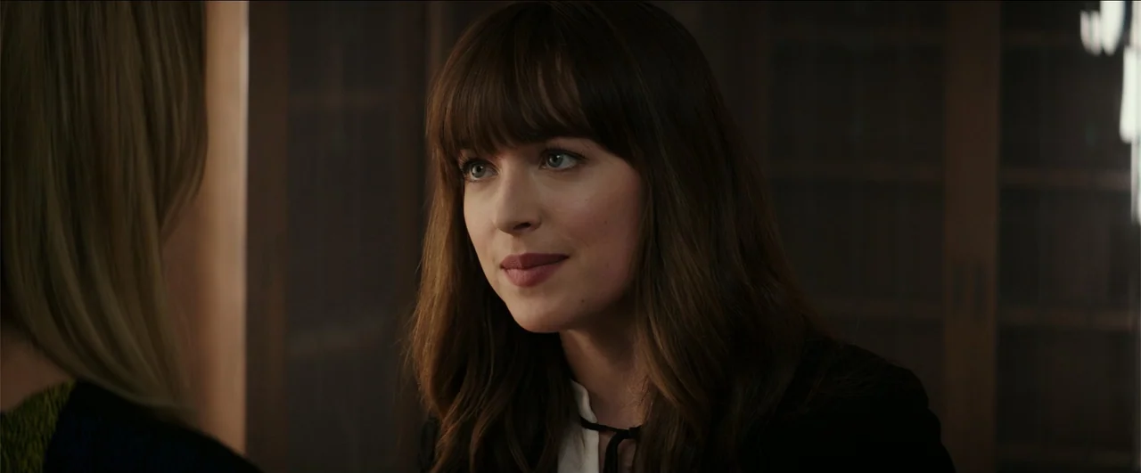 Fifty Shades Freed (2018) movie still: closeup — An interior space features wooden shelving units visible in the blurred background. A young woman…