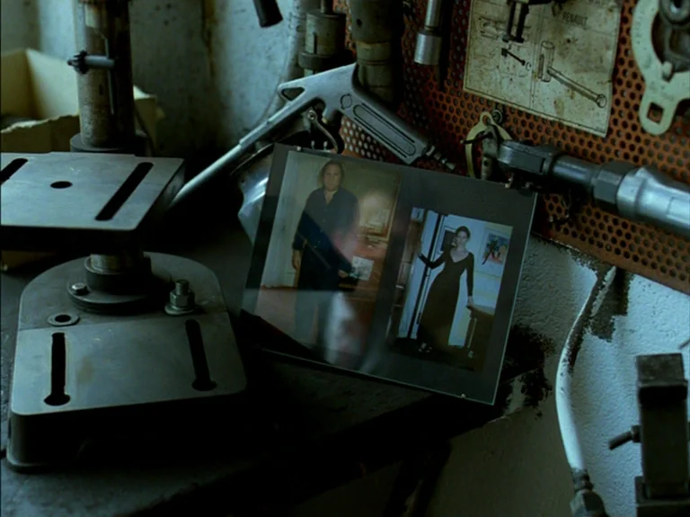 Helas Pour Moi (1993) movie still: closeup — A cluttered workshop workbench holds tools and a framed photograph of two people. The photograph sits…