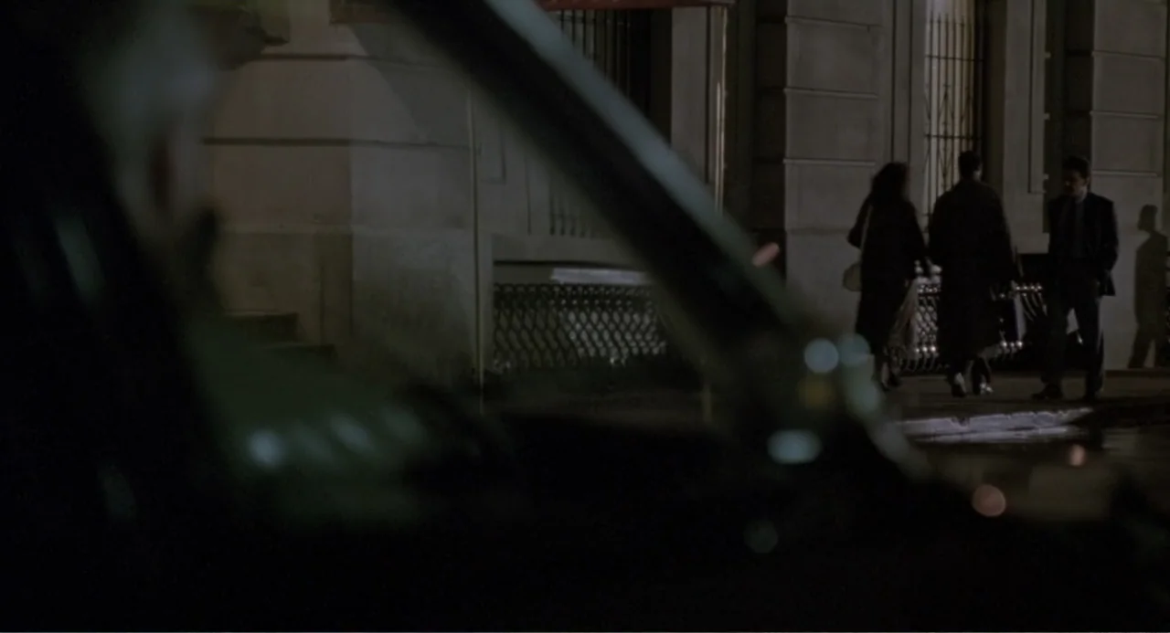 F/X2 (1991) movie still: medium — An urban exterior at night featuring a stone building façade with iron-grated windows. Three people gather on the…