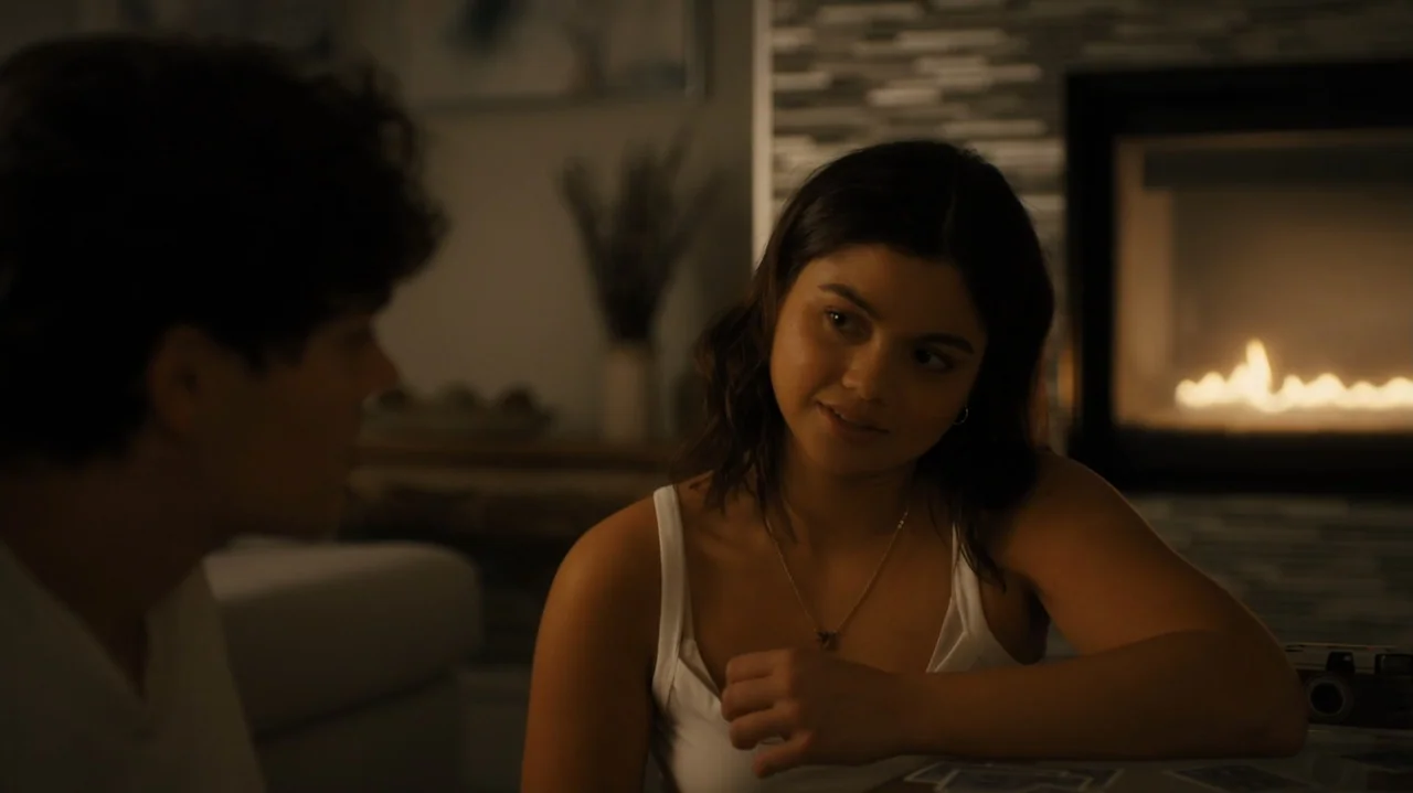 Sidelined: The QB and Me (2025) movie still: medium — An interior living room features a lit fireplace against a dark stone wall. A young woman in a…