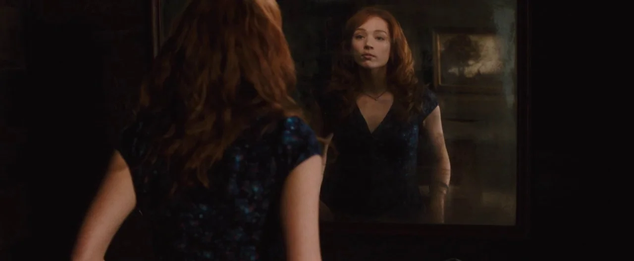 The Cabin In The Woods (2012) movie still: medium — A dimly lit space containing a large wall mirror with a dark frame. A young woman with red hair…