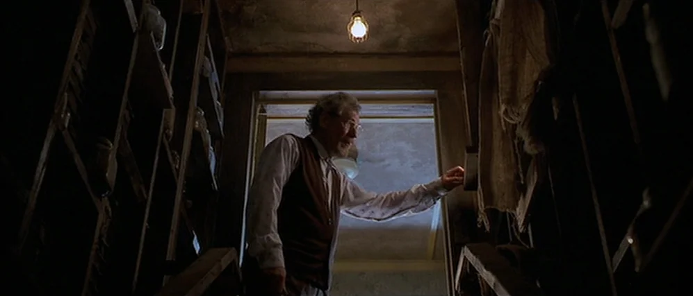 Apt Pupil (1998) movie still: medium — A dimly lit storage room features narrow wooden shelves packed with glass jars. An elderly man stands on…