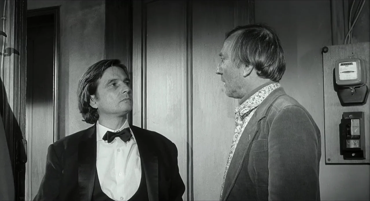 The Bohemian Life (1945) movie still: medium — A narrow interior space with plain wooden doors and an electrical meter on the wall. Two men stand…