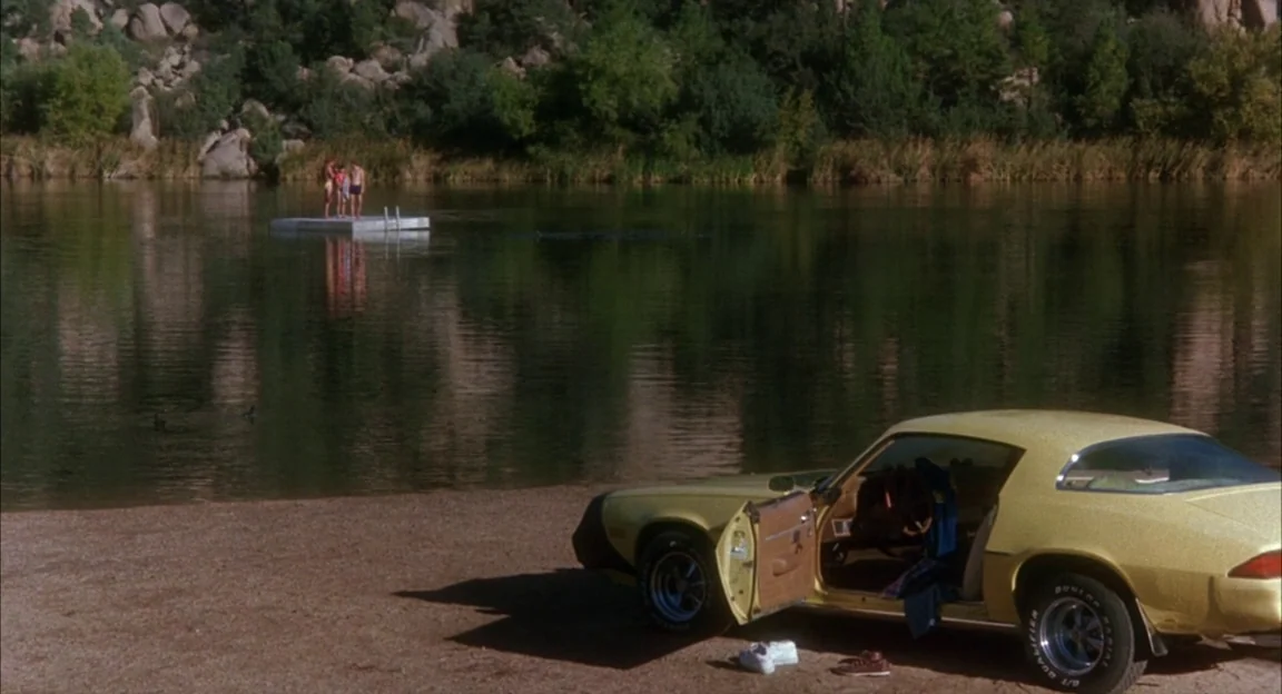 Creepshow 2 (1987) movie still: wide — A yellow vintage muscle car sits parked on a sand bank near a still lake. Three people stand on a white…